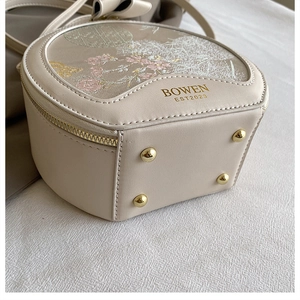 Detail of beige semi-circle bag with floral embroidery and gold metal bottom studs