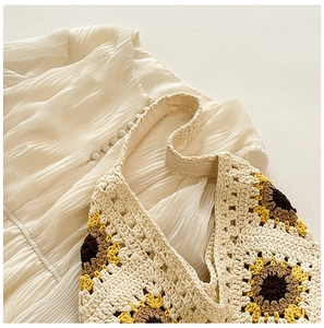 Gros plan détaillé du sac en crochet avec tournesols posé sur une robe beige plissée