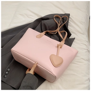 Detail of pink tote bag with embossed pattern and heart pendant on a soft background