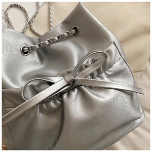 Detalle del bolso de cubo plateado con textura agrietada y adorno de lazo metálico