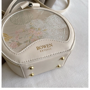 Detail view of round off-white crossbody bag with floral embroidery and gold rivets