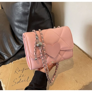 Detail of pink quilted crossbody bag with heart-shaped decor and silver chain strap