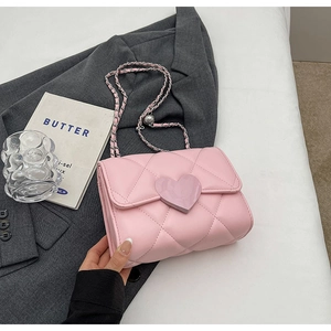 Detailed shot of pink quilted crossbody bag with heart buckle on a grey blazer