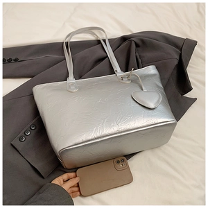 Detail of silver metallic crinkled tote bag with heart pendant on a grey blazer background