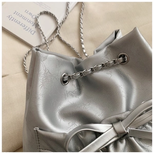 Detalle de bolso tipo cubo plateado con textura de grietas y lazo decorativo con cadena
