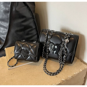 Macro view of quilted black leather shoulder bags with heart-shaped buckles on stone