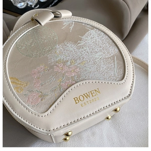 Close-up of circular embroidery handbag with pink floral patterns and gold metal studs