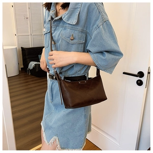 Detail of dark brown dumpling bag with diamond quilted texture on denim dress