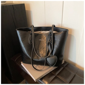 Detail of black faux leather tote bag with pleated texture and heart-shaped pendant charm