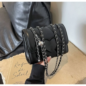 Detail of black quilted leather mini bag featuring silver heart buckle and chain strap