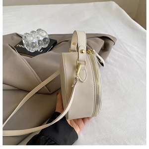 Detail view of round cream PU leather bag with gold zipper and adjustable strap
