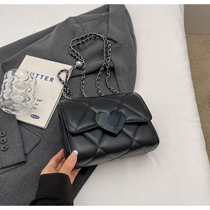 Detailed close-up of quilted black leather bag with glossy heart-shaped buckle and chain strap