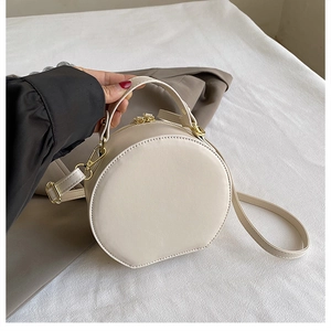 Close-up of circular cream leather bag featuring gold hardware and a top handle strap