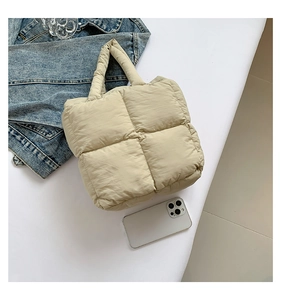 Flat lay of cream quilted puffer tote bag with thick handles beside denim jacket