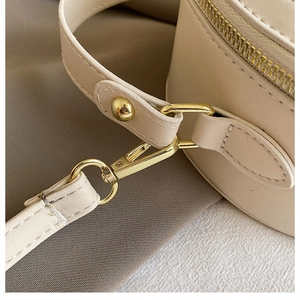 Close-up of golden metal hooks and fine stitching on the cream leather round handbag