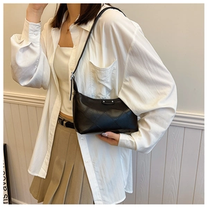Detail of black quilted faux leather dumpling bag shown as a crossbody on model in white shirt