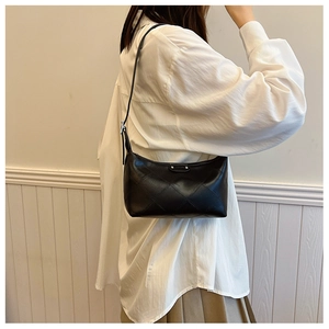 Detail of black quilted shoulder bag featuring classic diamond texture and silver buckle