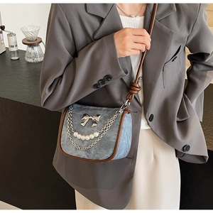 Close-up of a blue and brown shoulder bag with pearl chains and silver bow detail
