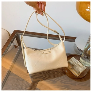 Detail of quilted cream baguette bag with adjustable strap and oval metallic logo