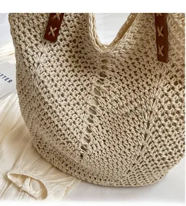 Detail of hollow crochet straw tote showing brown faux leather handles and cross stitching