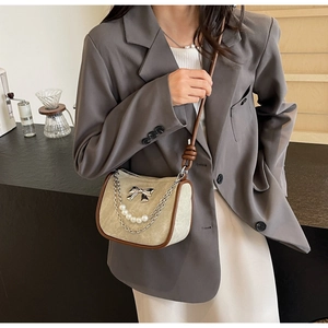 Close-up of beige suede shoulder bag with silver bow, pearls and chain detail