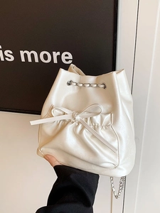 Bolso tipo cubo blanco crema con lazo, cordón de cadena plateada y bolsillo frontal plisado
