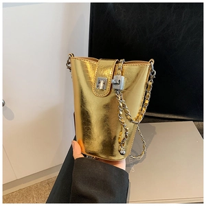 Détail du sac seau doré brillant avec chaîne en métal tressé et fermoir rotatif sécurisé