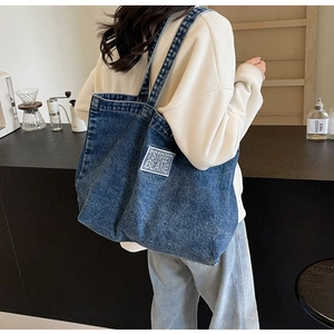 Detail view of washed denim tote bag featuring white logo patch and sturdy shoulder straps