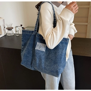 Detailed close-up of blue denim tote bag with 7STREET 6LANE patch shown on model