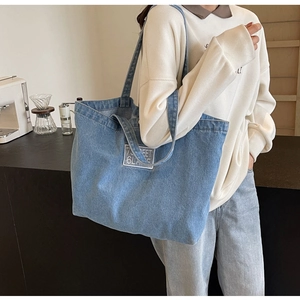 Detail of a large blue denim tote bag worn by a model in a modern cafe setting