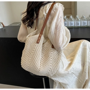 Detail of hand-woven straw tote with brown leather strap and decorative cross stitching