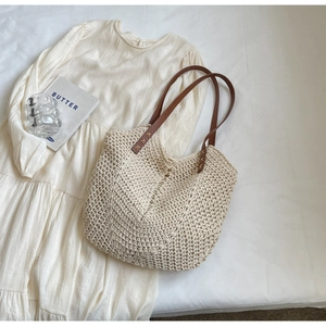 Minimalist woven straw tote bag with brown leather handles on white bedding backdrop