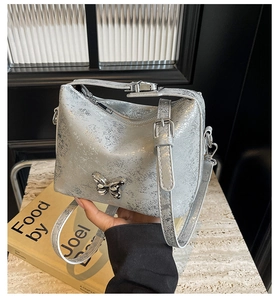 Detail of silver metallic bucket bag with butterfly ornament and adjustable strap
