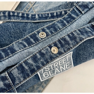 Detail of washed denim tote bag featuring white contrast stitching and metal snap buttons