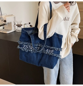 Vue détaillée d'un sac cabas en jean bleu marine avec bords effilochés et texte blanc au café