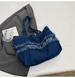 Détail d'un sac cabas en denim bleu foncé avec texte imprimé et bords effilochés