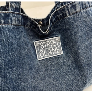 Detail of the embroidered patch and metal snap closure on a denim tote bag