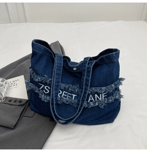 Détail du cabas en denim bleu avec bords effilochés et broderie artistique blanche