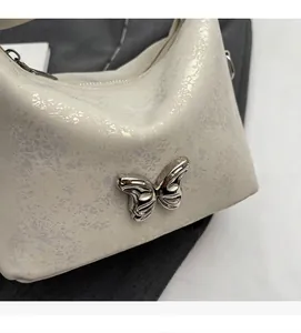 Detail of white bucket bag with cracked texture and silver metal butterfly ornament