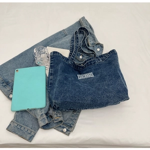 Flat lay of blue denim tote bag with white woven label on clean white fabric background