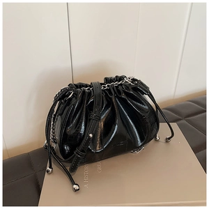 Detailed view of black patent leather bucket bag with pleats and silver chain strap