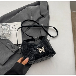 Detail of black crackle-leather bucket bag featuring a silver butterfly metallic ornament