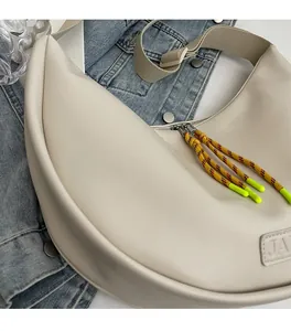 Détail du sac demi-lune crème avec tirette en corde d'escalade sur fond de veste en jean