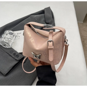 Close-up of pink bucket bag with metallic texture, butterfly clasp, and adjustable strap