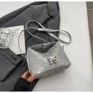 Detailed close-up of a silver patent leather bucket bag with a metal butterfly clasp