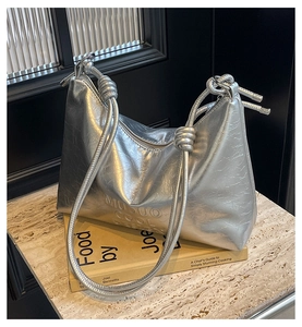 Macro detail of silver metallic hobo bag featuring knotted strap and embossed logo texture