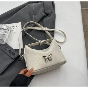 Detail of a creamy white crossbody bag with a metallic silver butterfly buckle on a desk