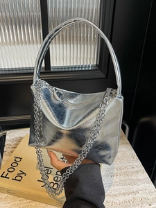 Silver wrinkled metallic handbag with chain strap displayed on a stone surface