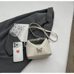 Detail of cream-colored crossbody bag featuring a silver metal butterfly ornament on a grey blazer