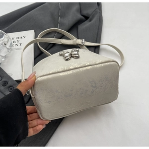 Close-up of white bucket bag with silver crackle texture and metal butterfly detail